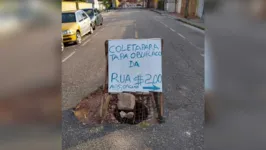 Uma placa colocada no local do buraco serve para sinalizar e ainda avisar sobre a 'vaquinha'