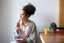 Portrait of a happy young woman sitting at home with pen and paper