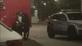 Fardado, PM se curva para beijar mulher ao lado de viatura.