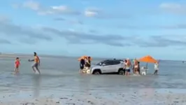 Pessoas tentam ajudar motorista a retirar o carro que estava sendo engolido pelo mar