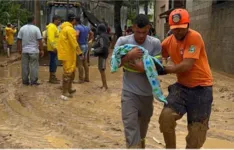 Morador com criança de colo recebe ajuda do Corpo de Bombeiros para deixar área atingida por enxurrada, em São Sebastião (SP).