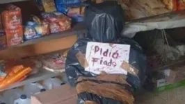 No peito do “cadáver”, a mensagem macabra alerta: “Pediu fiado”, sugerindo que o cliente não acabou bem.