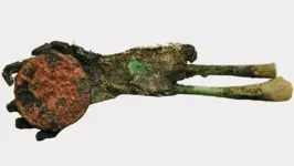 Mão mumificada verde segurando uma moeda de cobre