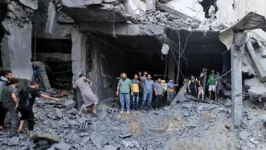 Civis palestinos procuram sobreviventes nos escombros de um edifício atingido durante o bombardeio