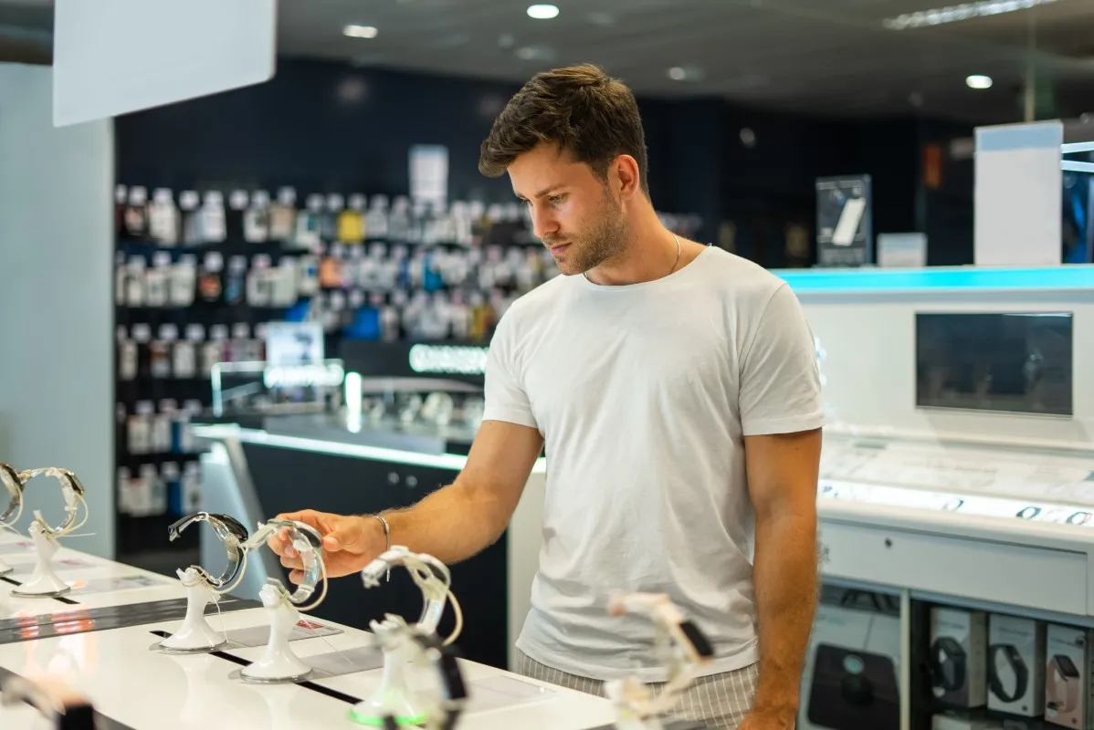 Young male customer examining modern smartwatch while choosing electronic gadgets in modern shop