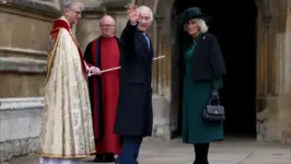 Rei Charles III acena para o público ao descer do carro com sua esposa, a rainha Camilla.