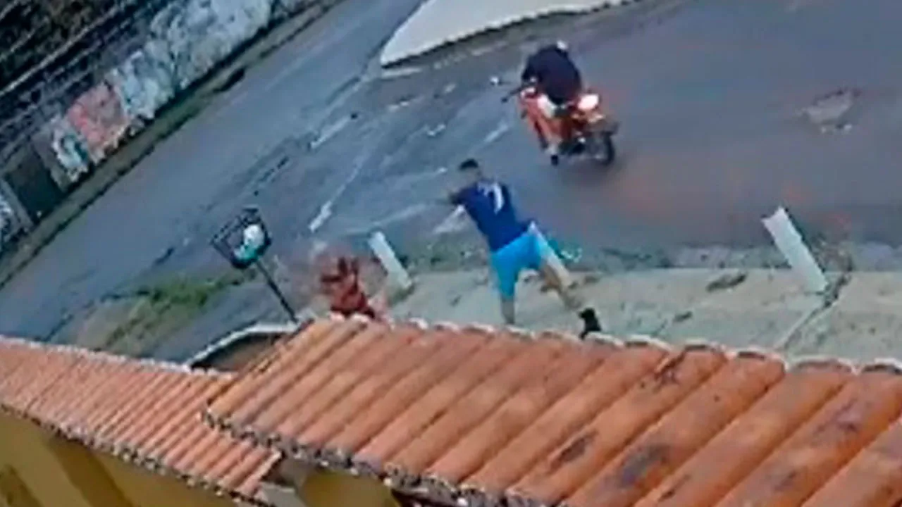 Nas imagens, é possível ver a vítima caminhando pela calçada quando dois criminosos em uma moto se aproximam