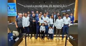 Weliton Ribeiro Gomes, o Timbó, ladeado por autoridades durante o recebimento da Moção de Aplausos na Câmara Municipal.