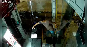 Câmera de segurança flagra o momento exato em que o criminoso arromba a porta de vidro do estabelecimento.