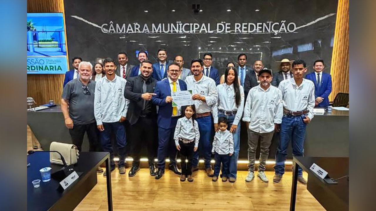 Weliton Ribeiro Gomes, o Timbó, ladeado por autoridades durante o recebimento da Moção de Aplausos na Câmara Municipal.