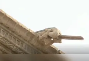 A peça em questão é uma escultura de pedra que representa um homem nu em posição agachada.