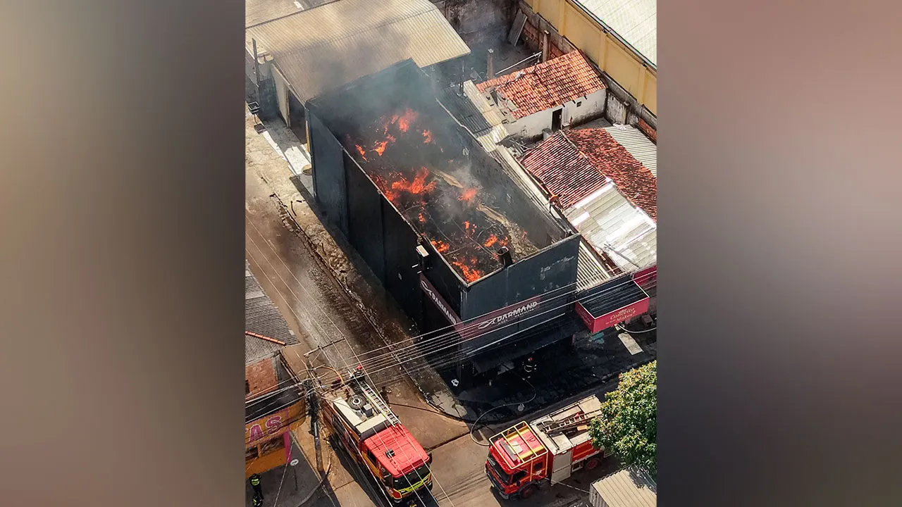 Bombeiros atuam no combate ao fogo enquanto parte do estoque retirado do imóvel permanece agrupado na calçada.