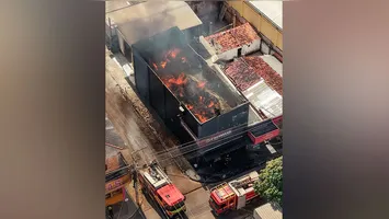 Bombeiros atuam no combate ao fogo enquanto parte do estoque retirado do imóvel permanece agrupado na calçada.