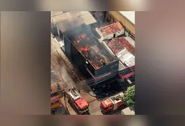 Bombeiros atuam no combate ao fogo enquanto parte do estoque retirado do imóvel permanece agrupado na calçada.