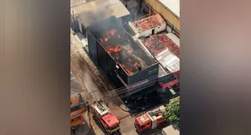 Bombeiros atuam no combate ao fogo enquanto parte do estoque retirado do imóvel permanece agrupado na calçada.