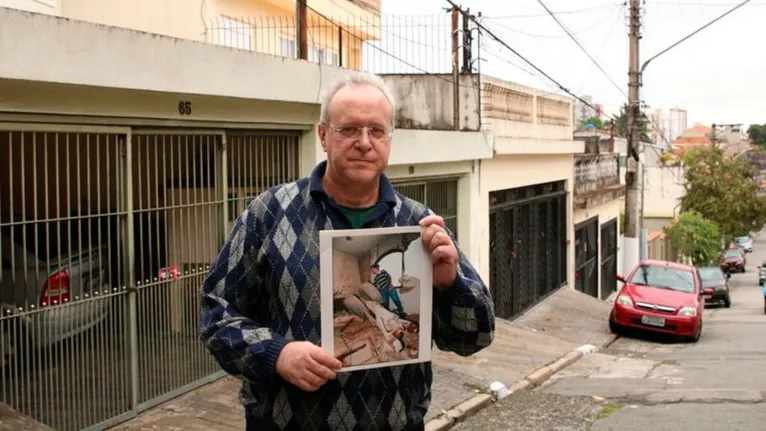 O jornalista Jorge Tadeu da Silva, um dos afetados pelo acidente com o avião modelo Fokker 100 da TAM que vitimou 99 pessoas em 1996, segura foto de como ficou a casa dele na rua Luís Orsini de Castro, no Jabaquara.