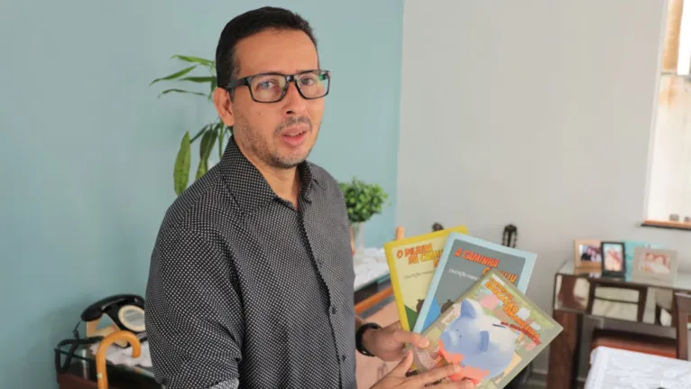Professor Alexandre Damasceno exibe os três livros que escreveu sobre educação financeira, direcionados para crianças, jovens e adultos