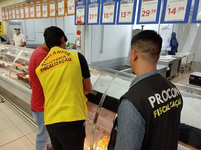 Fiscais aplicando papel de interdição no balcão de frios do supermercado.