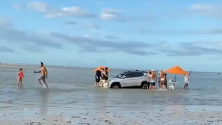 Pessoas tentam ajudar motorista a retirar o carro que estava sendo engolido pelo mar