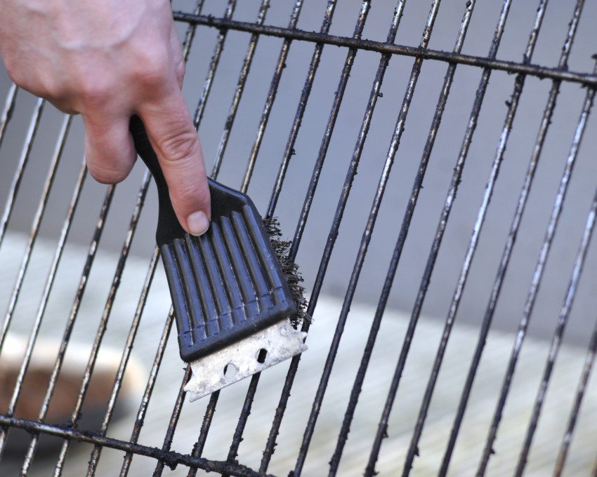 human hand is cleaning the grill rost with scrubber