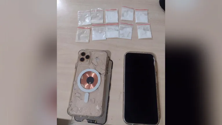 O iPhone 11 que foi jogado no muro e os papelotes de drogas encontrados próximos ao aparelho jogado