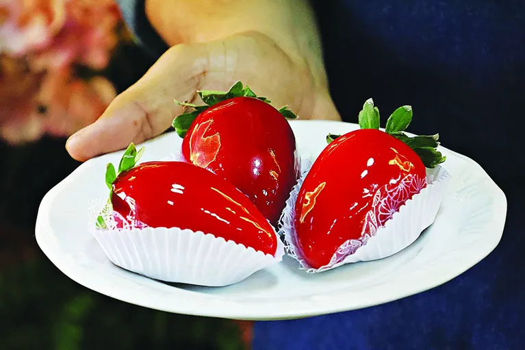 O doce é um morango envolto por brigadeiro e coberto por uma fina camada de açúcar caramelizado vermelho, assim como a conhecida maçã do amor.