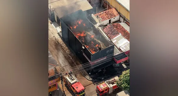 Bombeiros atuam no combate ao fogo enquanto parte do estoque retirado do imóvel permanece agrupado na calçada.